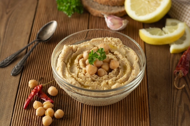 Homemade hummus. Woman hands with hummus in bowl, olive oil, lemon and spices.