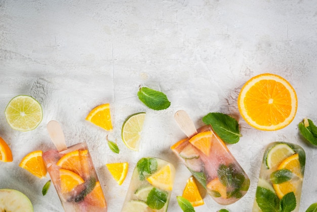 Homemade ice cream. Frozen drinks. Fresh fruits, citrus. Popsicles of red, white sangria, lemonade or mojito. With oranges, lime, mint, apples. White stone table, ingredients. top view 