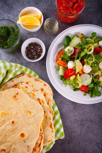 Домашняя индийская лепешка наан со свежим салатом и соусами на обеденном столе