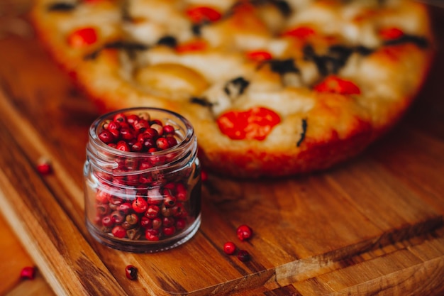 Homemade Italian Focaccia, with tomato, pink pepper and olive oil on a rustic wooden background.