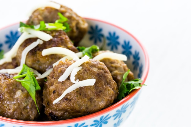 Homemade Italian meatballs garnished with cilantro and parmesan cheese in a small bowl.