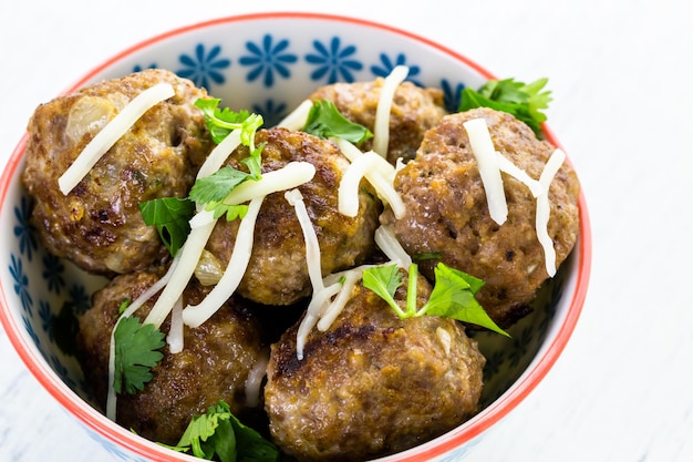 Homemade Italian meatballs garnished with cilantro and parmesan cheese in a small bowl.