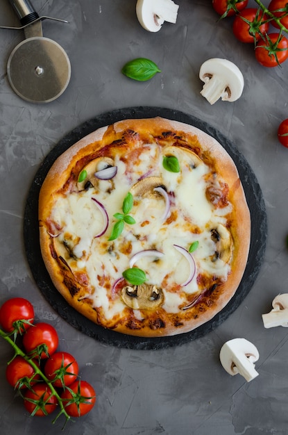 Homemade Italian vegetarian pizza with tomato sauce, mushrooms, cheese, onions and basil on a stone on a dark background.