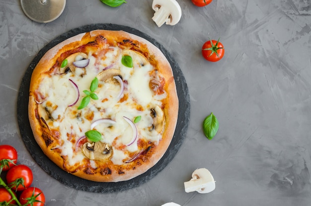 Homemade Italian vegetarian pizza with tomato sauce, mushrooms, cheese, onions and basil on a stone on a dark background.