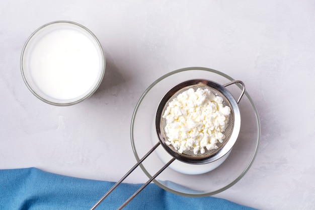 Photo homemade kefir stands in a glass, next to kefir grains on a gray background