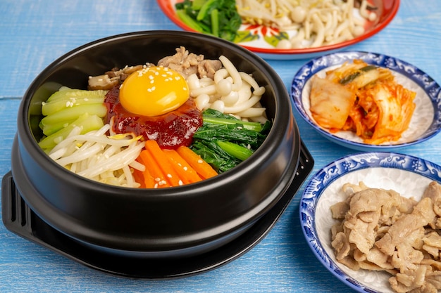 비빔밥이라는 수제 한국식 잡곡밥이 반찬을 배경으로 뜨거운 돌솥에 담겨 나옵니다.