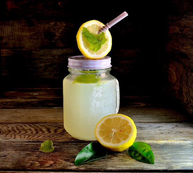 Homemade lemonade in a glass with a straw with mint and lemon on a wooden table.