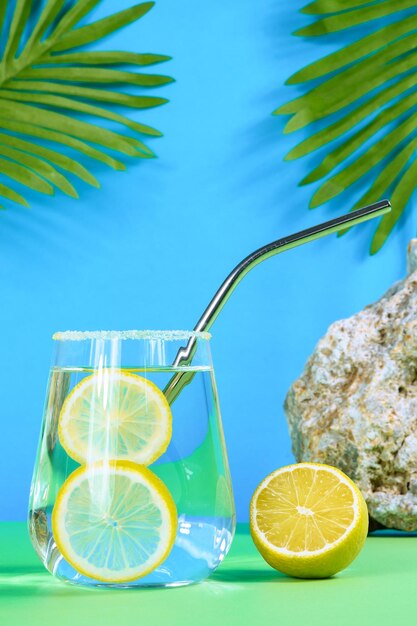 Foto limonata fatta in casa su sfondo verdeblu con foglie di palma pietra e limone