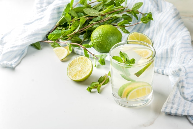 Homemade lemonade or mojito cocktail with fresh lime and mint leaves, white marble , 