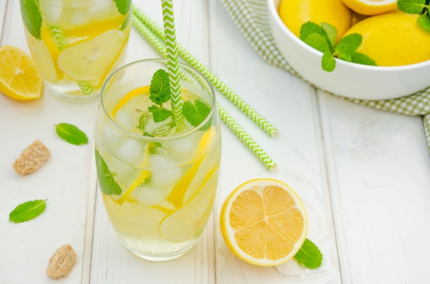 Домашний лимонад с дольками лимона, мяты и коричневого сахара в стакане со льдом на белой деревянной поверхности