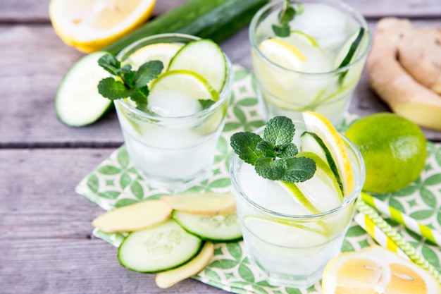 Homemade lemonade with lime, mint, ginger, cucumber and ice on a wooden background