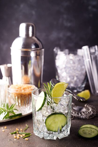 Homemade lime lemonade with cucumber, rosemary and ice on a dark concrete background and s