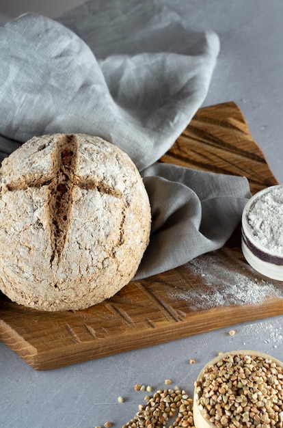 Homemade loaf of freshly baked green buckwheat bread lies on a wooden kitchen board with gray linen napkin. Harmless, wellness, gluten free healthy baking for vegans and vegetarians.Alternative bread