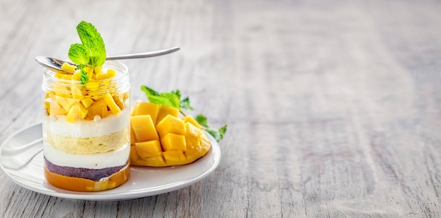 Homemade mango dessert cheesecake trifle mouse in a glass jar on a light wooden background