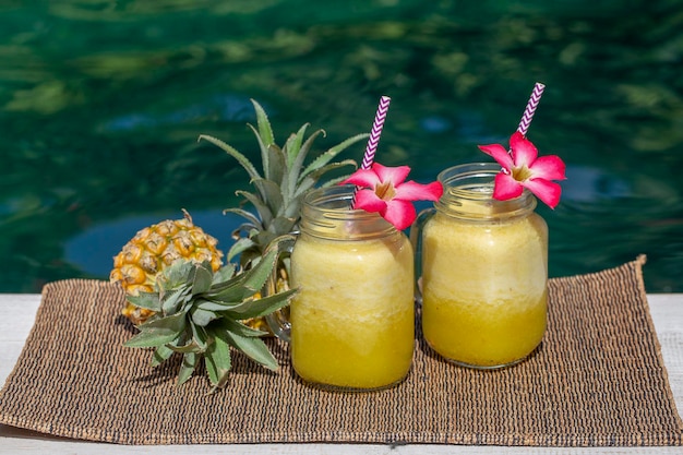 Homemade mango and pineapple smoothie made with coconut milk in two glass mug near swimming pool Island Bali Indonesia Refreshing tropical fruit drink