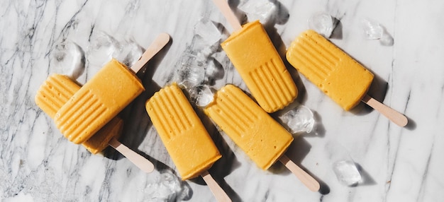 Homemade mango smoothie vegan popsicles over marble background wide composition