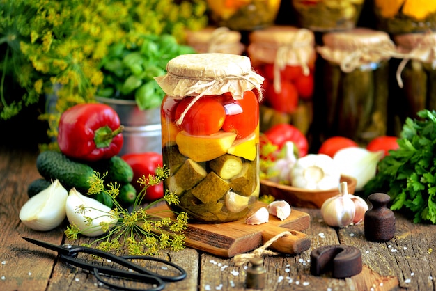 Homemade marinated assorted with tomato, cucumber and squash, dill, carrot, garlic and onion in a jar on an old wooden background. Rustic style.