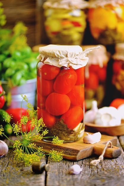 Homemade marinated tomato with dill, carrot, garlic and onion in a jar on an old wooden background. Rustic style