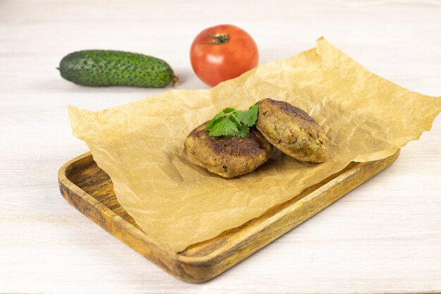 Homemade meat beef burger patties cutlet on wooden tray, baking paper on white tablewith vegetables, herb. Low carb diet concept. Close up. Selective focus. Copy space