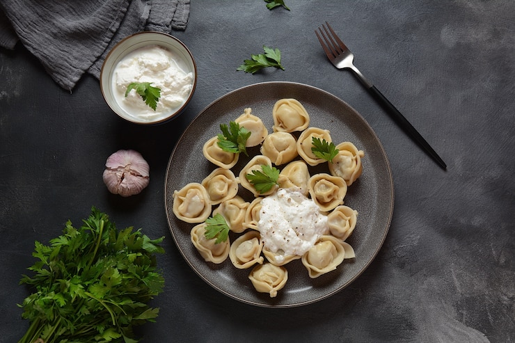 Домашние пельмени с мясом, подается со сметаной и свежей петрушкой на тарелке. (Русские пельмени)
