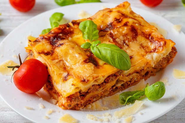 Homemade meat lasagna with fresh basil parmesan cheese and cherry tomato in a plate on white wooden