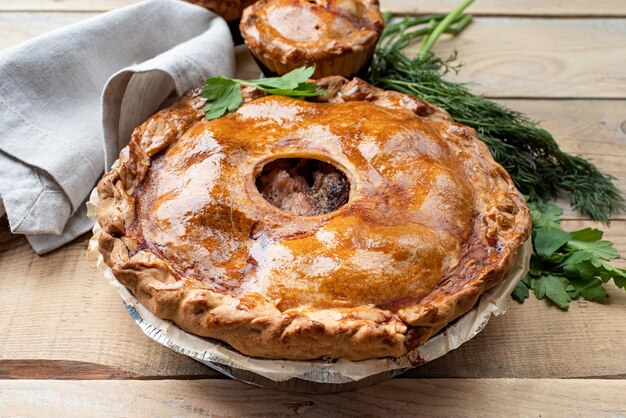 Homemade meat pie with greenery on wooden background