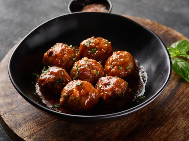 Homemade meatballs with tomato sauce and spices served in black plate on wooden board