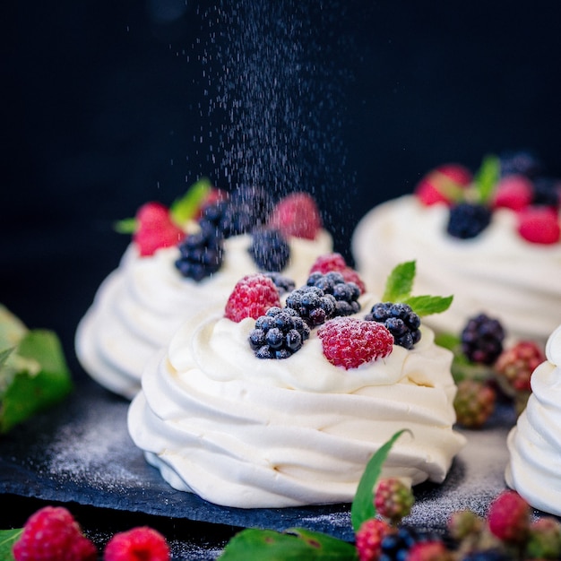 Homemade meringue basis for cake Pavlova with fresh blueberries and BlackBerry and powdered sugar on black concrete texture surface