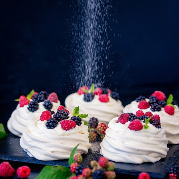 Base meringata fatta in casa per torta pavlova con mirtilli freschi e mora e zucchero a velo su fondo nero