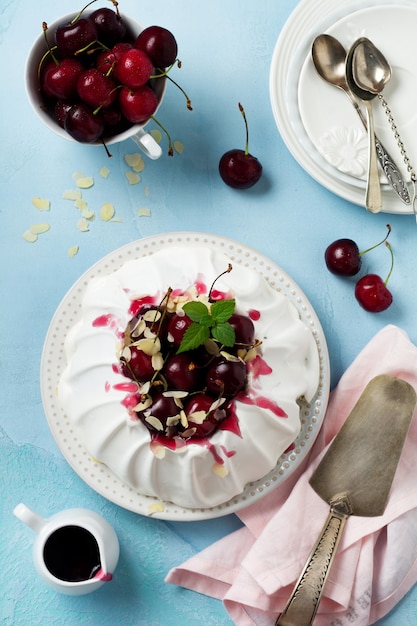 Photo homemade meringue cake pavlova with whipped cream, fresh cherry and sauce on light concrete