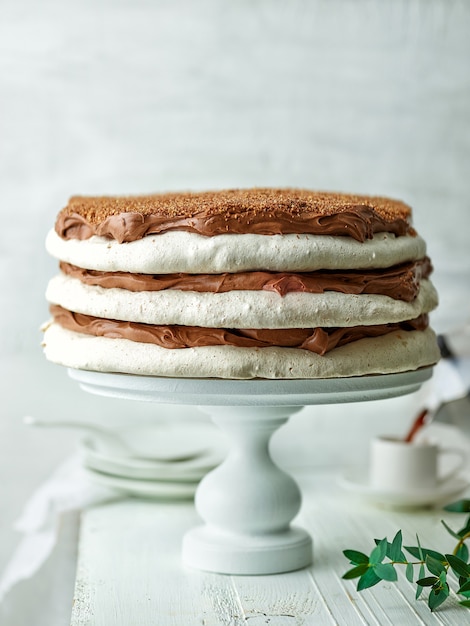 Homemade meringue and nut cake with chocolate cream on white wooden table