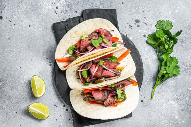 homemade mexican steak steet tacos with cilantro green sauce jalapenos and onion gray background top view