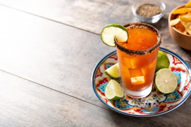 Homemade michelada cocktail with beer lime juicehot saucesalted rim and tomato juice on wooden table