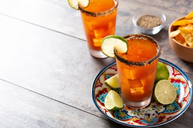 Homemade michelada cocktail with beer lime juicehot saucesalted rim and tomato juice on wooden table