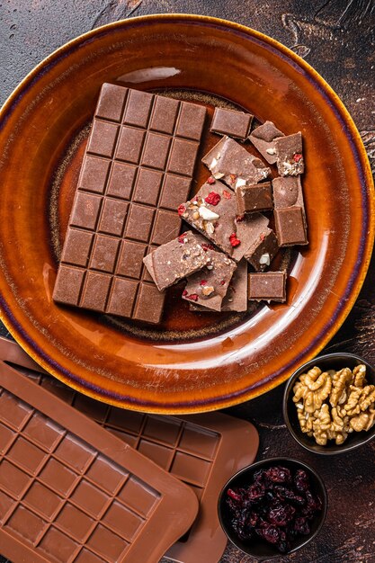 Homemade milk chocolate with hazelnuts, peanuts, cranberries and freeze dried raspberries on a rustic plate. Dark background. Top view.