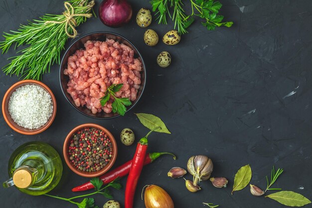 Homemade minced meat in a black bowl over dark slate or stone or concrete background with ingredients for making Top view with copy space