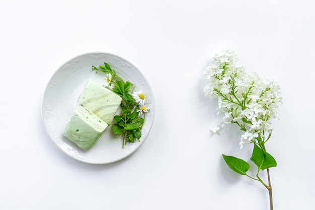 Homemade mint marshmallows on a plate with bouquet of garden plants, white lilac branch on white