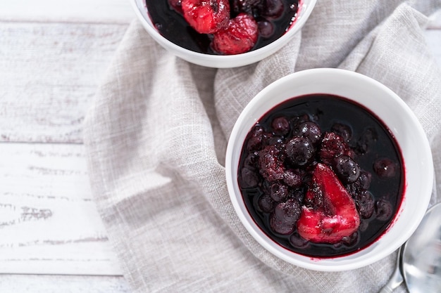 Homemade mix berry compote in small white bowls on a wooden table.