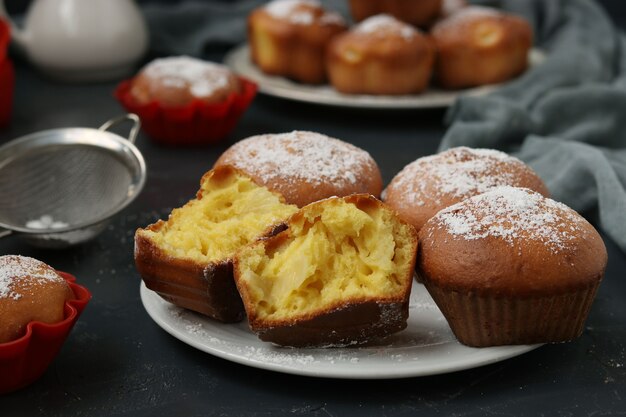 Homemade muffins with pineapple pieces, sprinkled with powdered sugar, arranged on a dark.