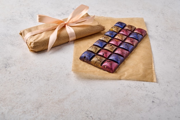 Homemade multicolored organic healthy chocolate bar on craft paper and gift tied with ribbon close