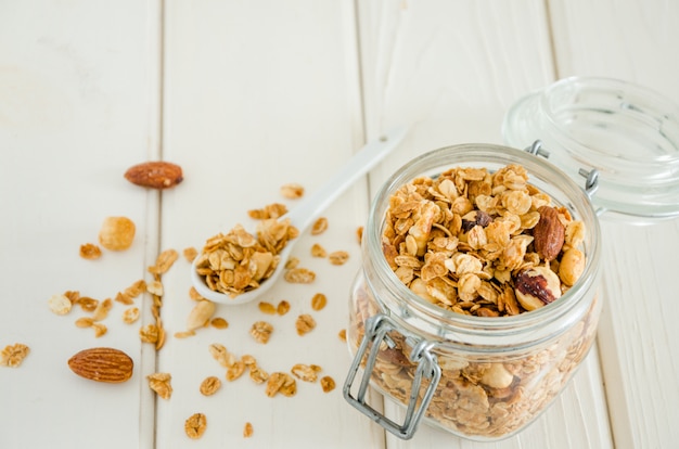 Homemade multigrain granola with a mixture of nuts in a jar on a white wooden surface