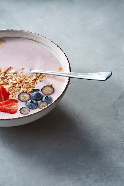 Homemade natural breakfast with granola strawberries, almonds, blueberries, fresh milk in a bowl on a gray background. Concept of natural healthy organic food.