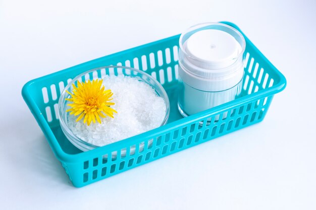 Cosmetici naturali fatti in casa, sale marino, un fiore e un vasetto di crema in un contenitore blu,