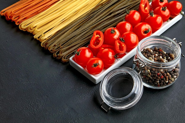 Homemade noodles in different colors from natural herbal ingredients an oblong bowl with tomatoes and red paprika and a glass jar with mixed peppers