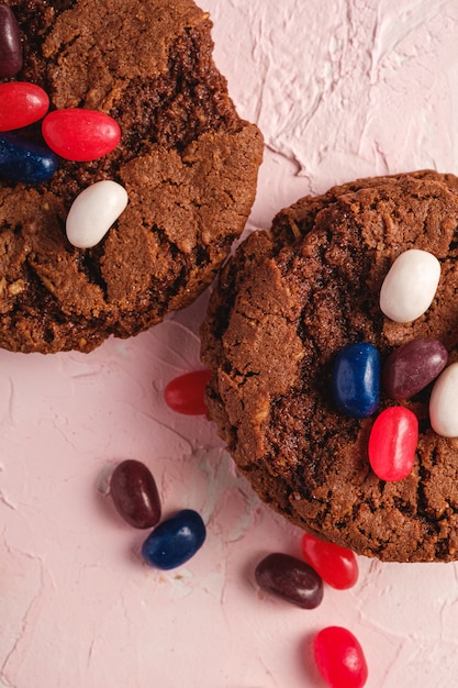 Homemade oat chocolate cookies with cereal with juicy jelly beans on  pink surface, top view macro