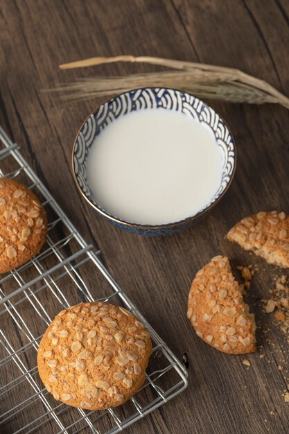 Homemade oatmeal biscuits with seeds and bowl of fresh milk on wooden table