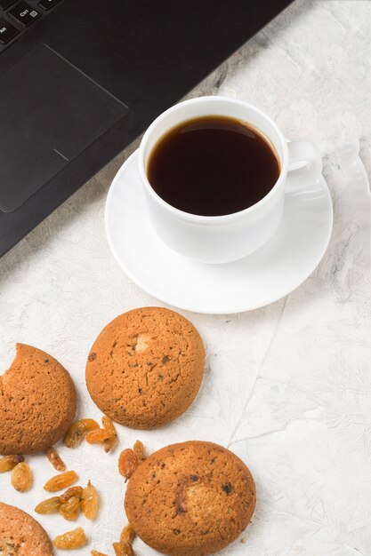 집에서 만든 오트밀 쿠키, 컵 커피와 가벼운 돌 표면에 노트북. 학생 평일