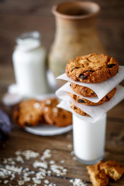 Домашнее овсяное печенье с орехами и изюмом и стаканом молока на темном деревянном фоне крупным планом
