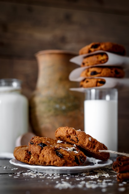 Homemade oatmeal cookies with nuts and raisins and glass of milk on dark wooden background