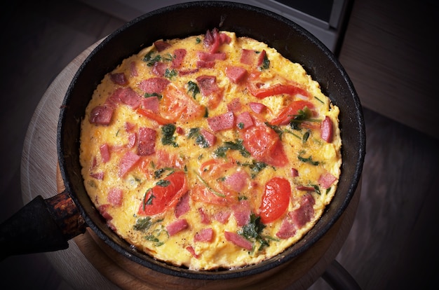 Homemade omelet with tomatoes and sausage in pan. Rustic breakfast